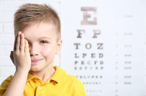 Happy boy covering his right eye ready for an eye exam at the optometrist office.