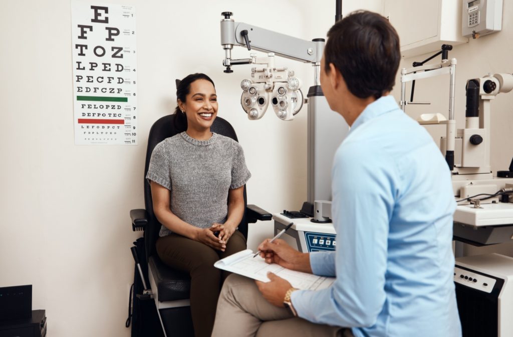 A patient sitting in an exam chair during an eye exam, smiling at the eye doctor sitting in front of her.