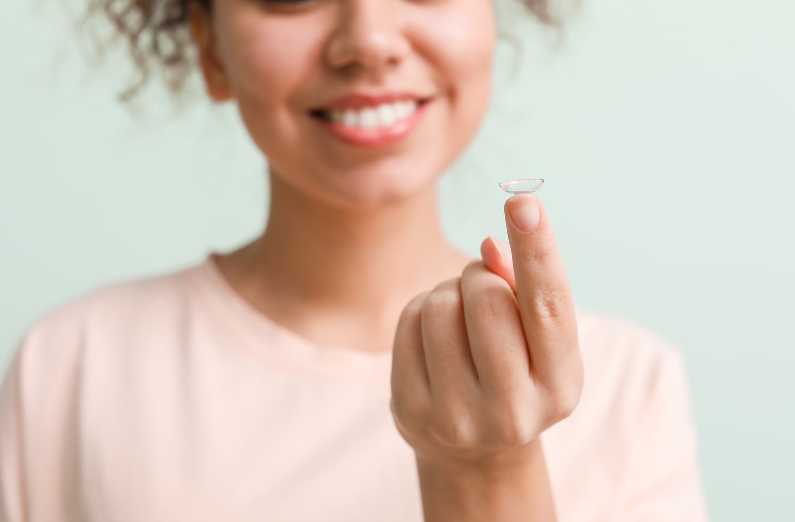 A young woman holding a contact lens on her index finger