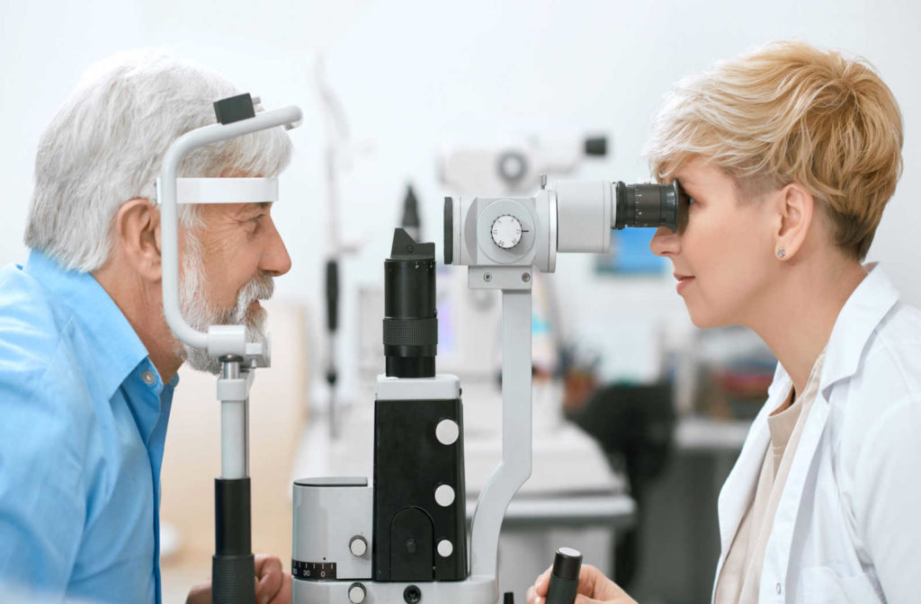 A female optometrist performs a slit lamp exam on an older male patient sitting across from her.