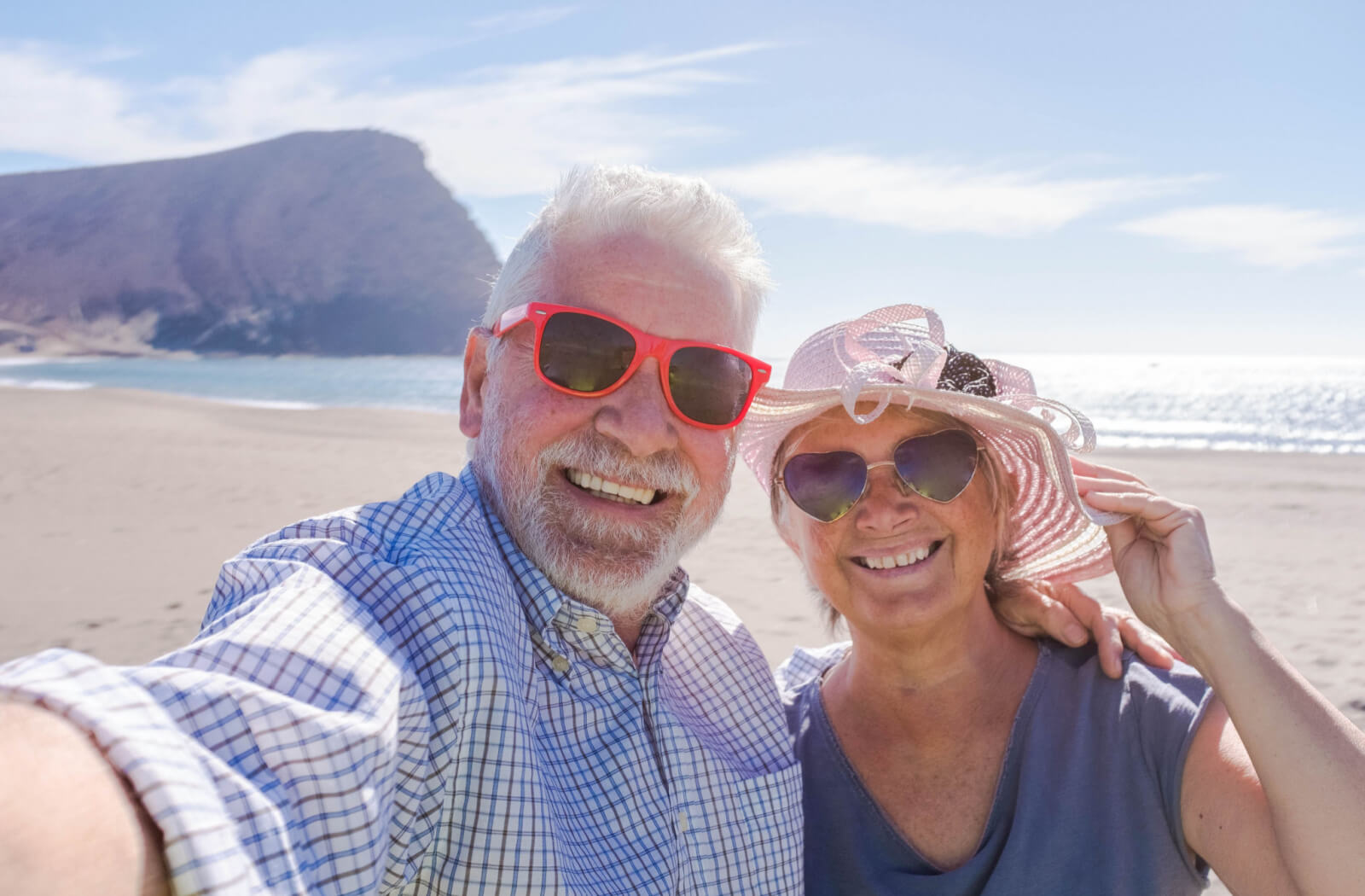 A male and female senior with their sunglasses on to protect their eyes from UV lights while enjoying the sun at the beach.