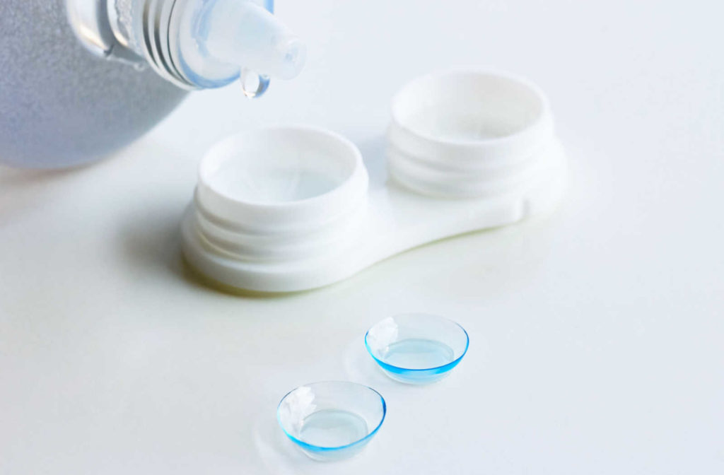 A contact lens solution dripping into a contact lens case with two contact lenses sitting on the counter