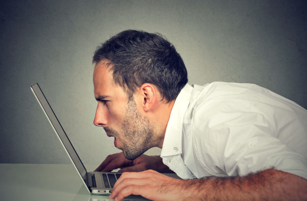 A young man moves closely in front of his computer. Having difficulty reading the text on the screen.