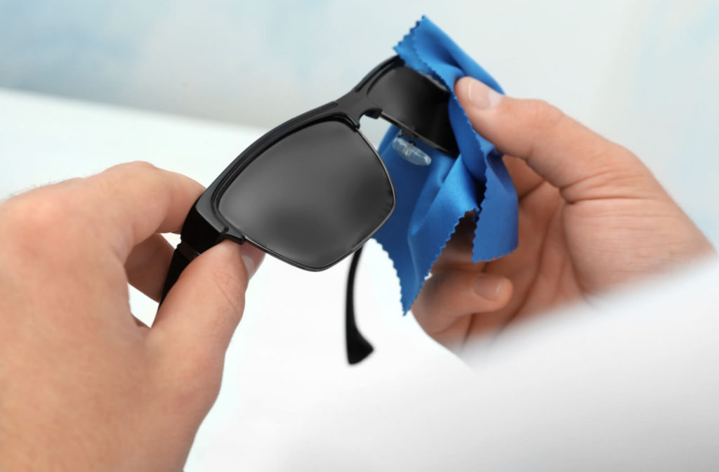 Hands of a man wiping sunglasses with a microfiber cleaning cloth.