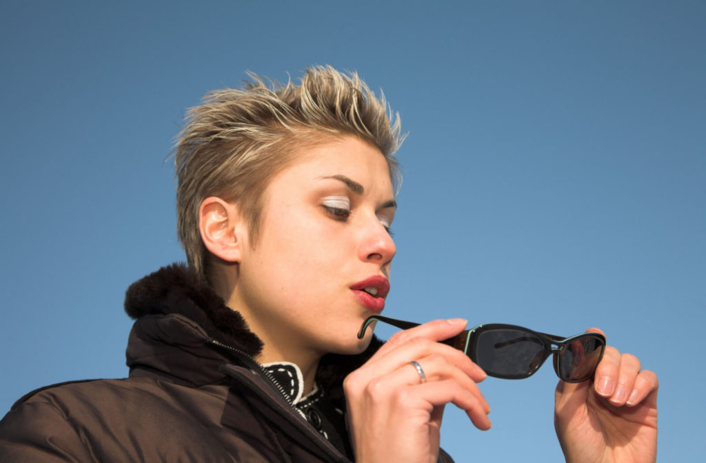 A woman outdoors is cleaning her sunglasses by blowing the dirt.