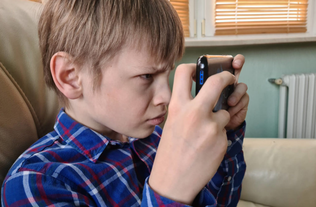 A child sitting on the couch and holding his smartphone very close to his face.