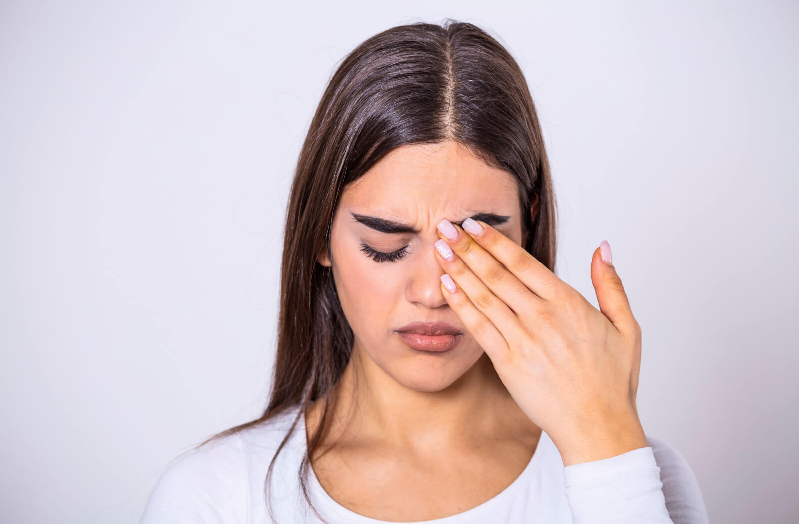A woman with eyelash extensions rubbing her left eye with her left hand.