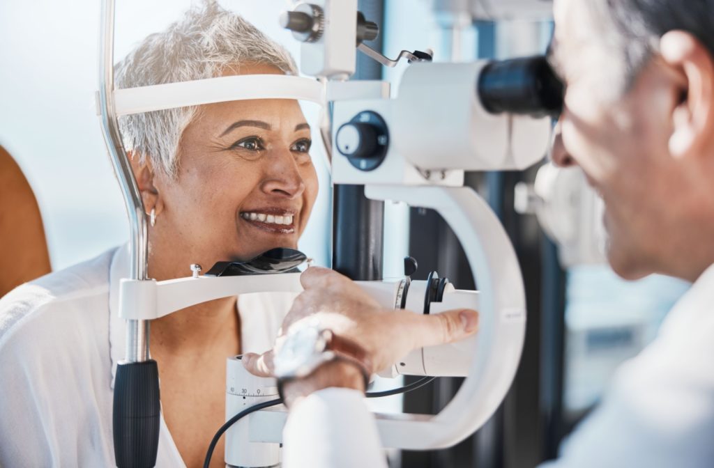 A senior woman smiling during a laser eye surgery consultation while an optometrist examines her eyes.