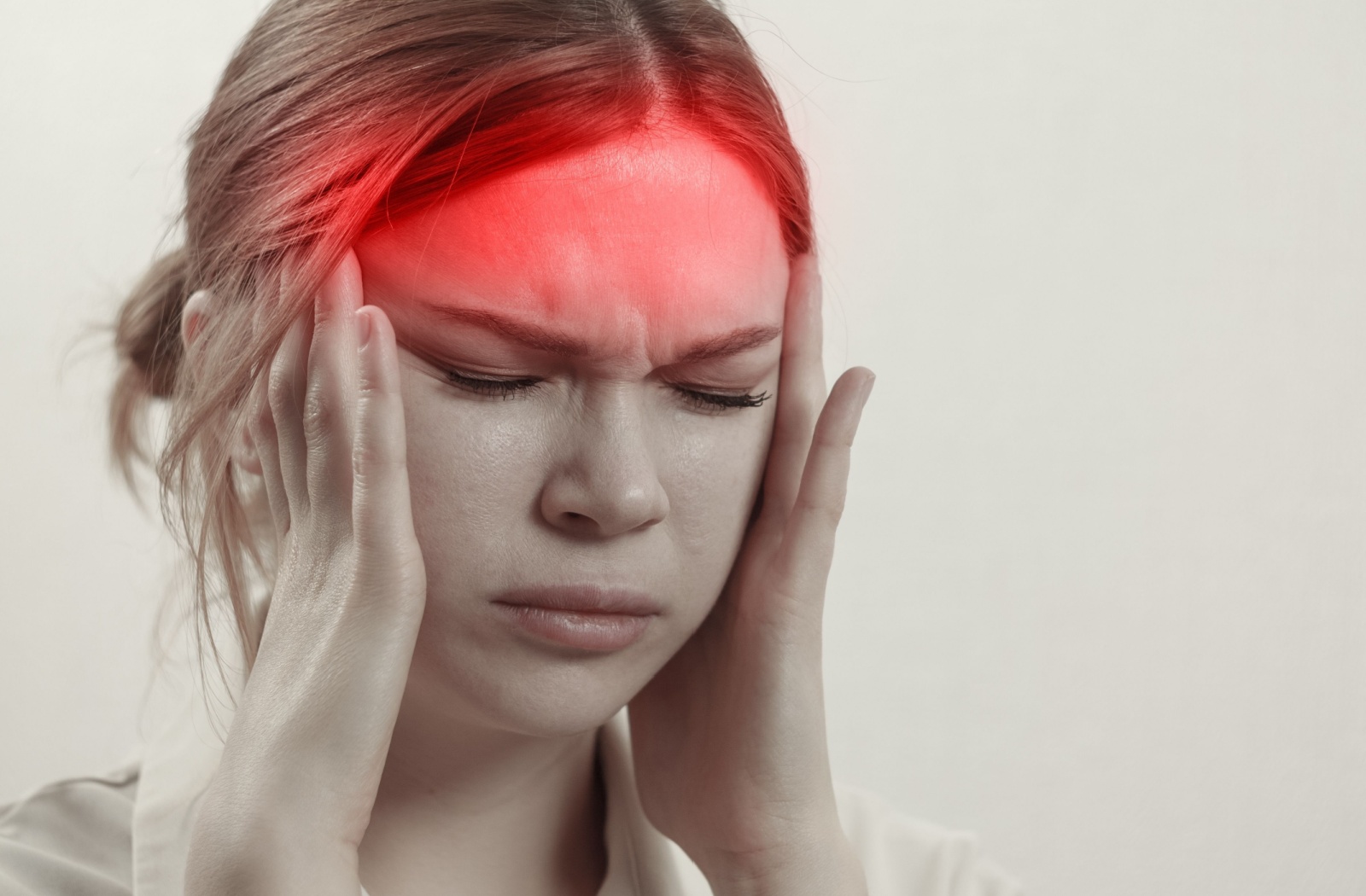 A young person with a headache closes their eyes and rubs their face with both of their hands, looking uncomfortable.