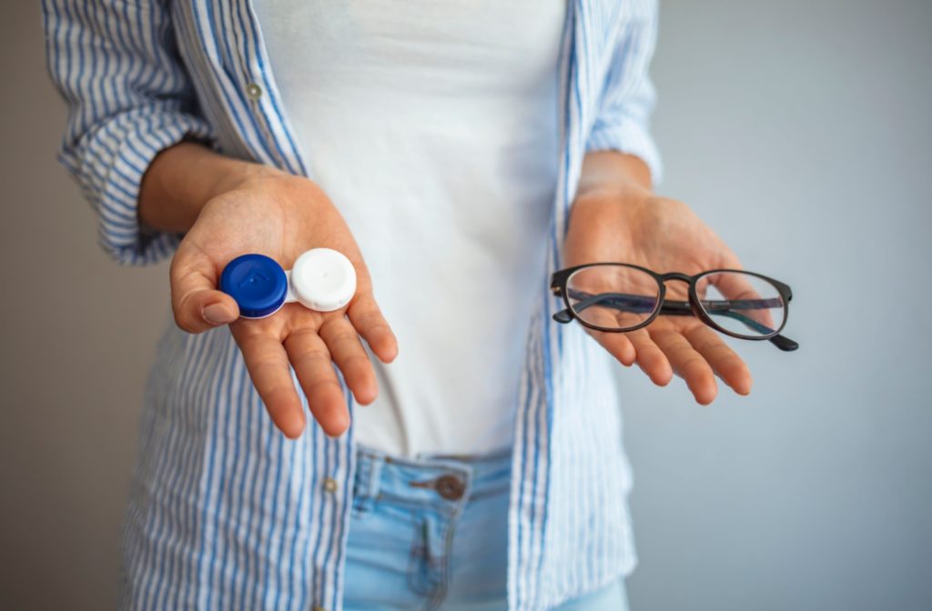 A person choosing an astigmatism treatment holds a pair of glasses in one hand and a contacts case in the other hand.