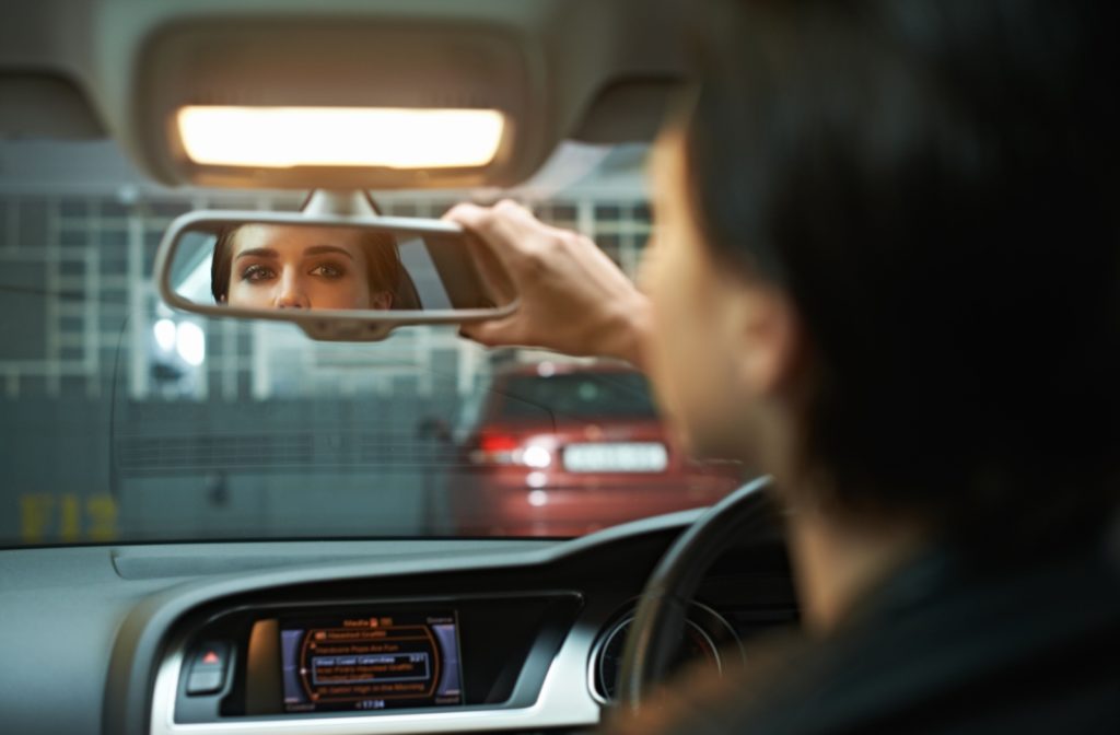 Person adjusting their rearview mirror in a car, focusing on their eyes in the reflection.