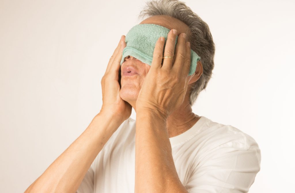 A senior sighs in relief after placing a warm washcloth over their eyes as a makeshift hot compress to relieve pain