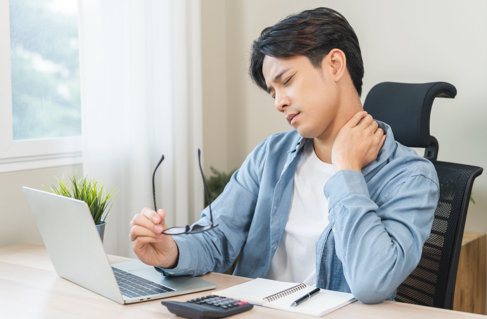 A person sitting at a desk, rubbing their neck due to pain related to eye strain and vision problems.