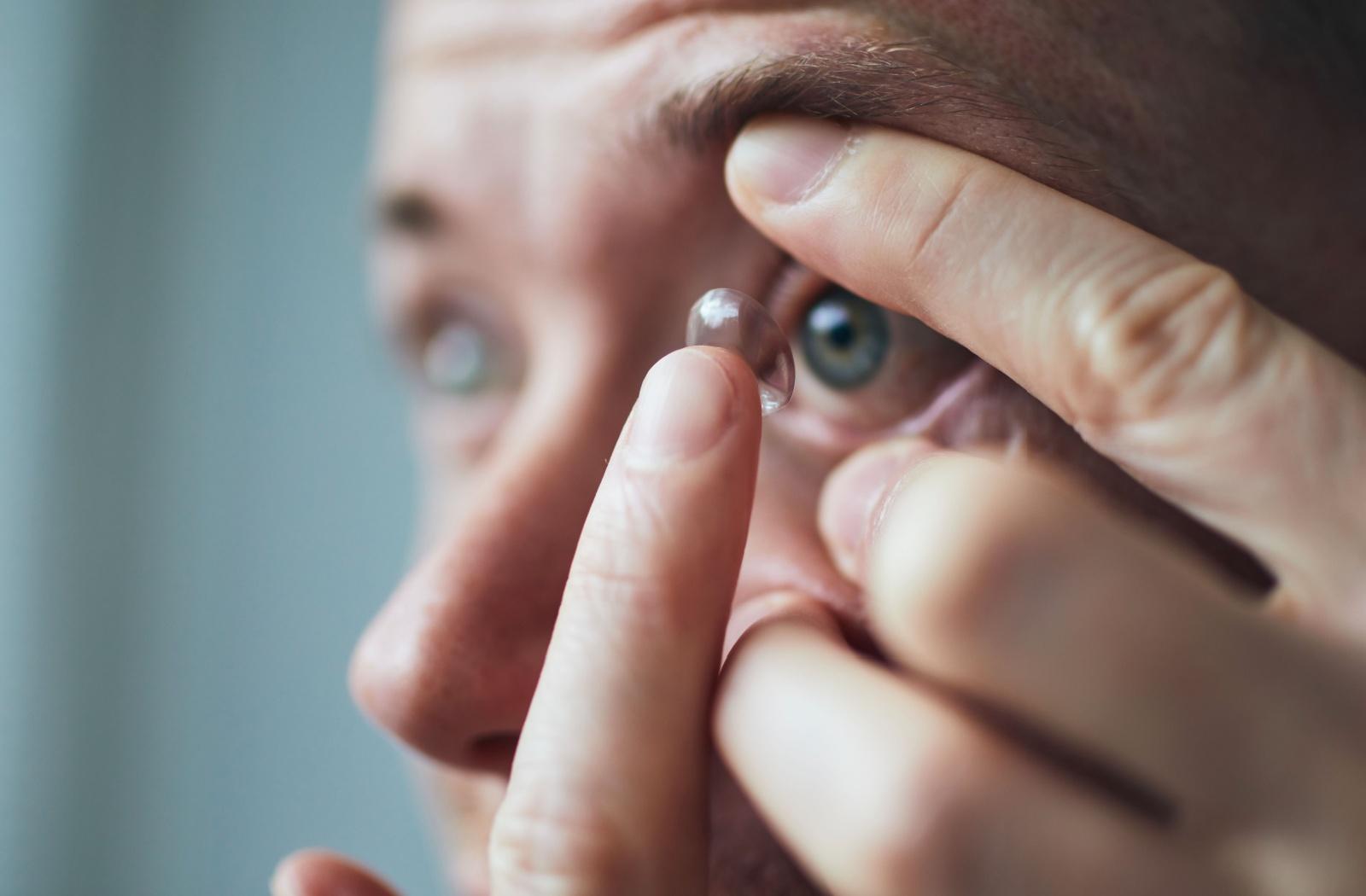 A close up of an adult inserting an ortho-k lens into their eye.